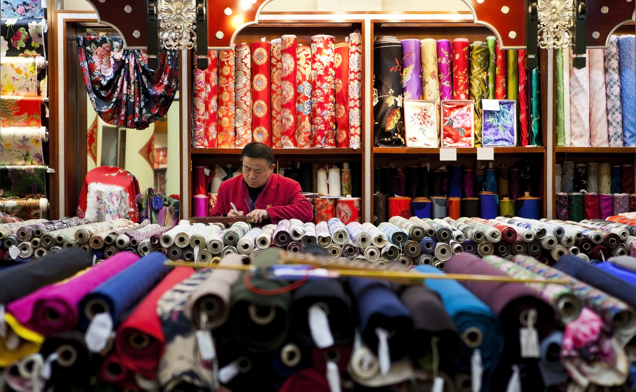 Silkebutikk med mange ruller silke, m�leb�nd og en mann