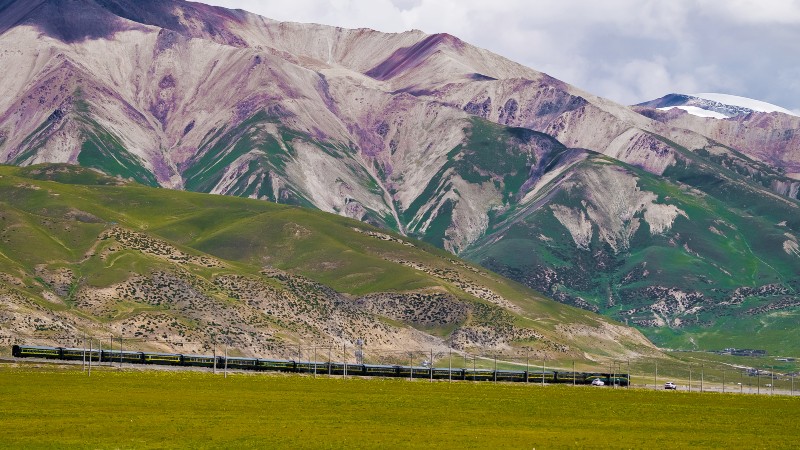 fjell, gr�nne �ser og et tog som slynger seg framover i landskapet