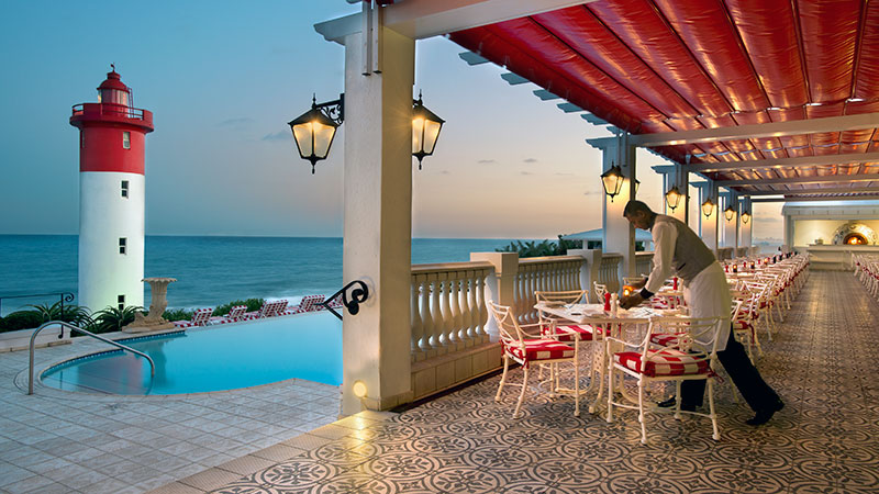 Terrasse ved bassenget p� Oyster Box Hotell, med fyrt�rnet og have i bakgrunnen 