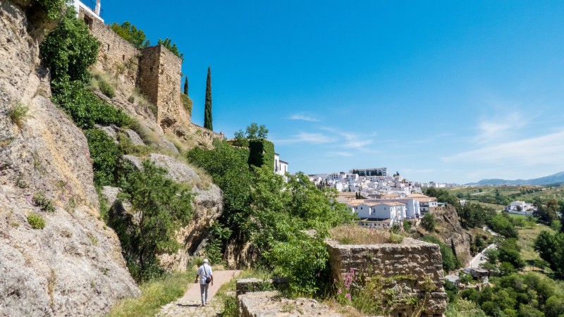 Ronda en mann som går på en sti med bygninger og en festning på toppen av fjellet